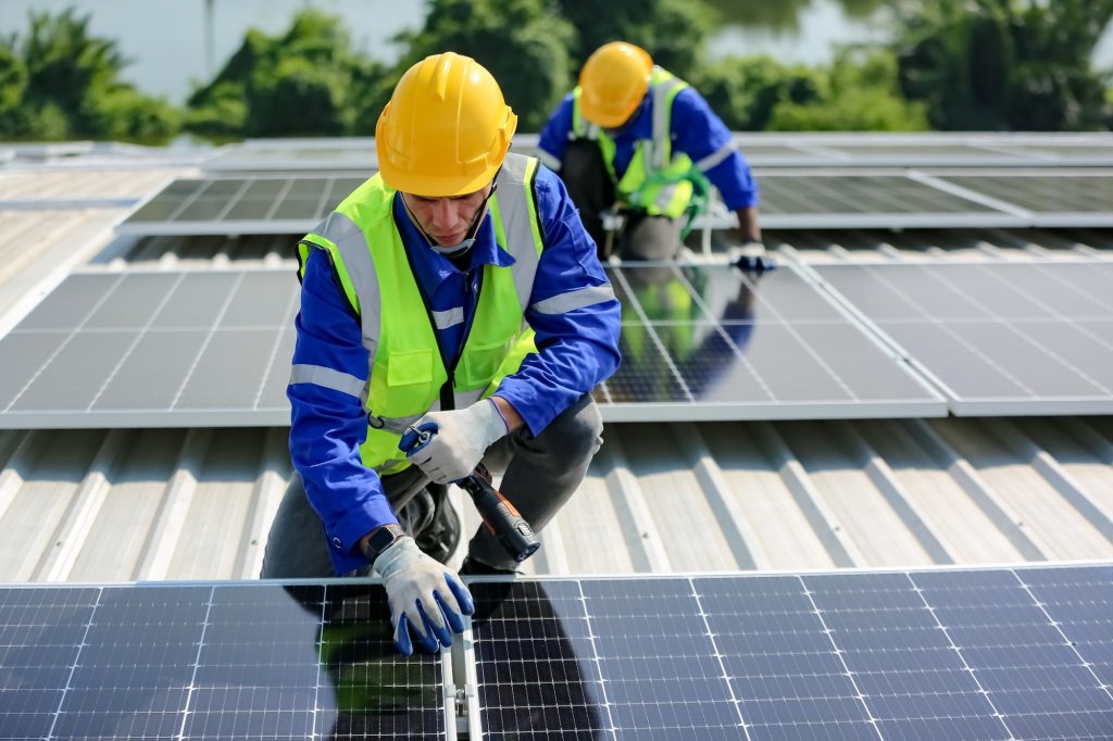 Solar panel installer installing solar panels on roof of warehouse